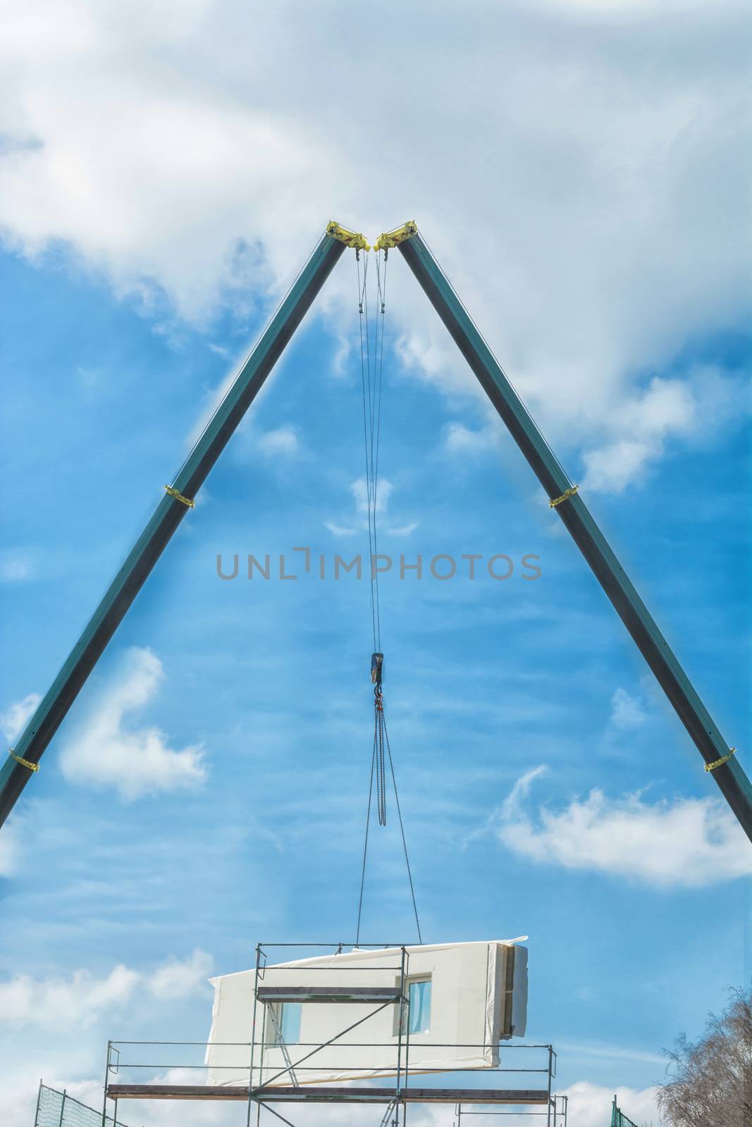 Two mobile construction cranes when delivering a prefabricated building. Concrete wall against blue sky.