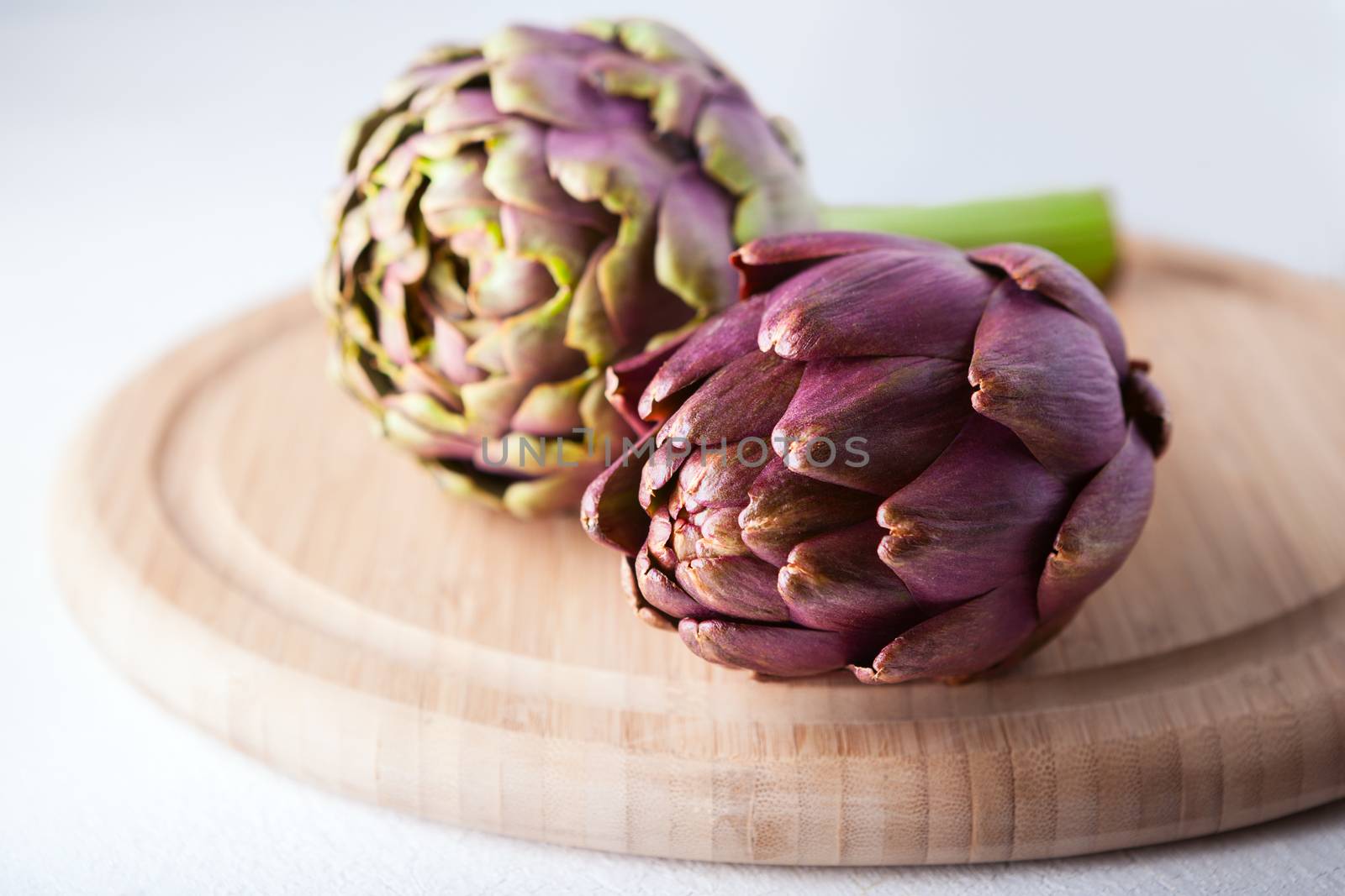 Two artichokes lying on a wooden plate.