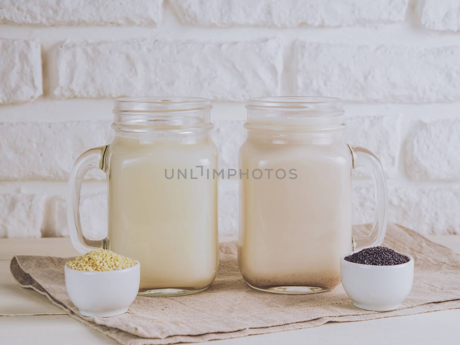 Close up view on two mason jar with vegan milk from sesame seeds and poppy seeds on white table. Copy space.