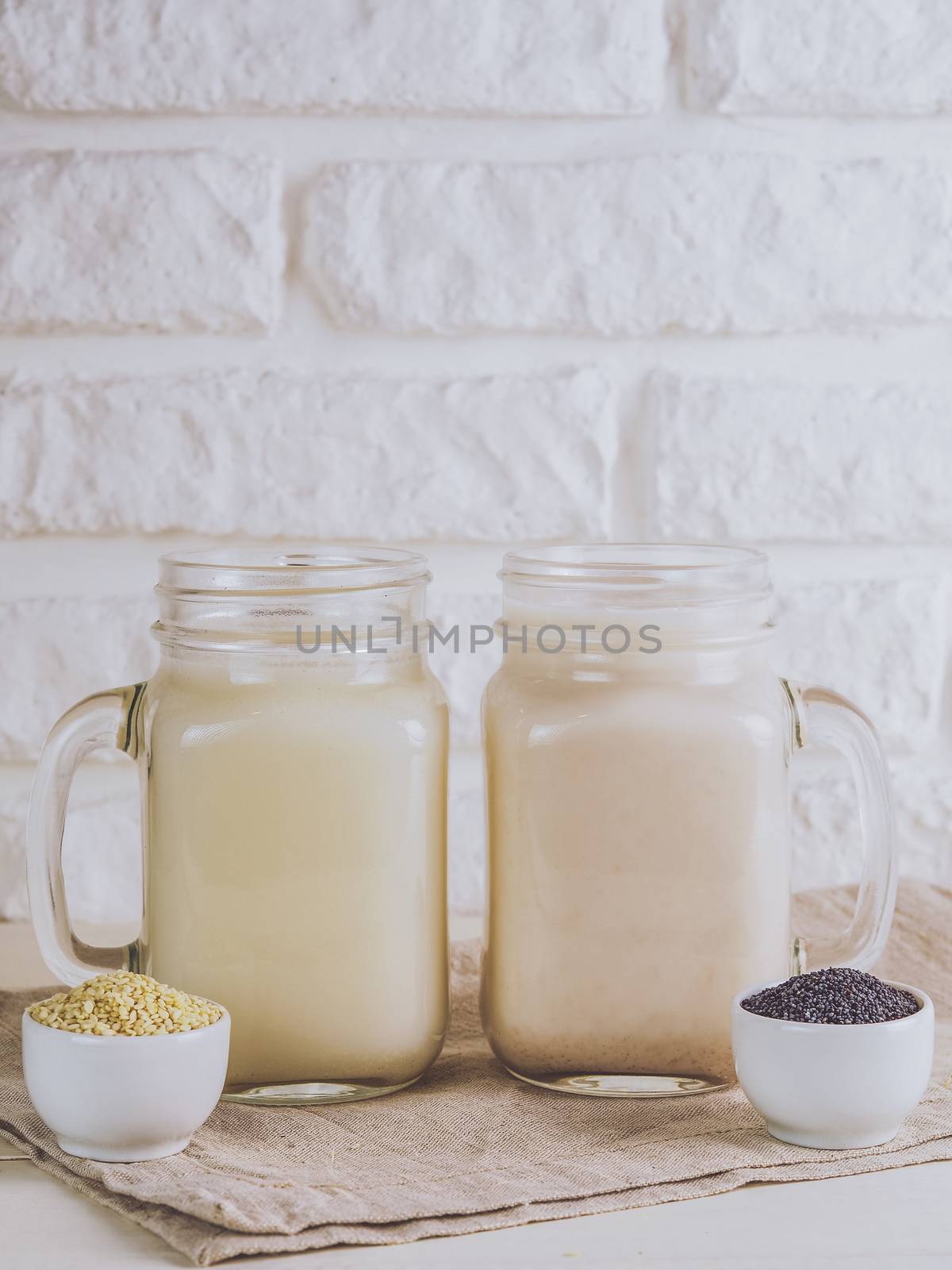 Close up view on two mason jar with vegan milk from sesame seeds and poppy seeds on white table. Copy space. Vertical.
