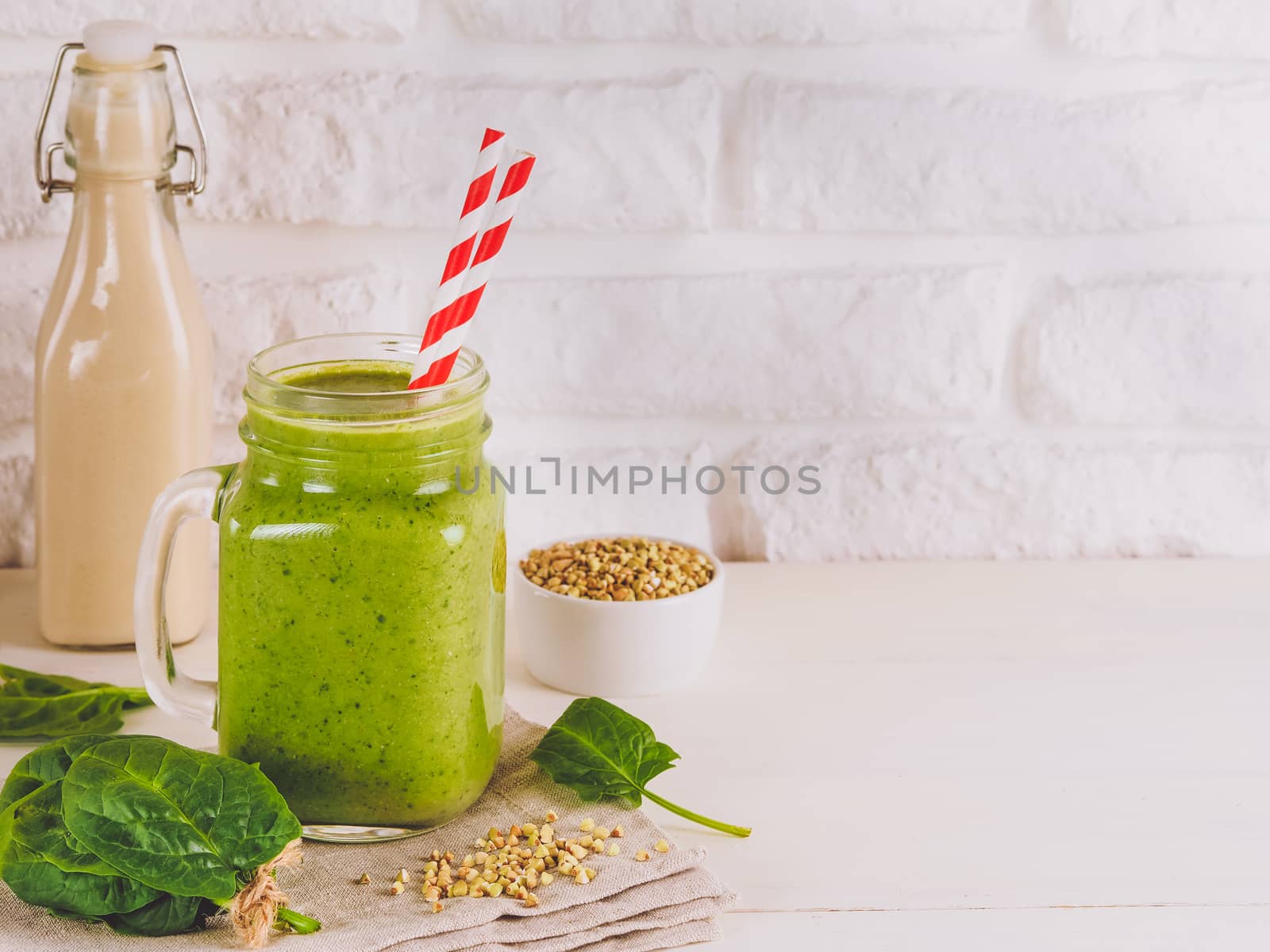 Close up view of green smoothie in mason jar on white table. Fresh green smoothie with green buckwheat, spinach and vegan milk. Copy space.