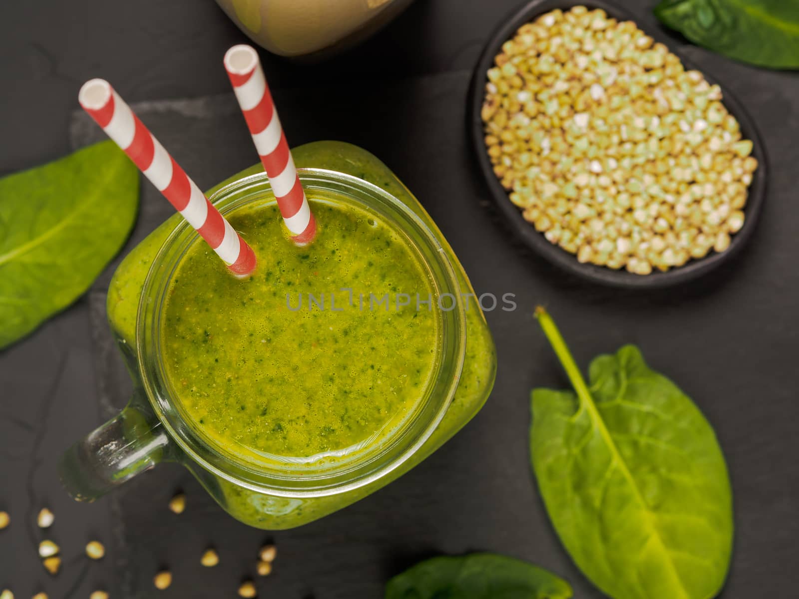 Top view of green smoothie in mason jar on black concrete background. Fresh green smoothie with green buckwheat, spinach and vegan milk. Copy space. Vertical.