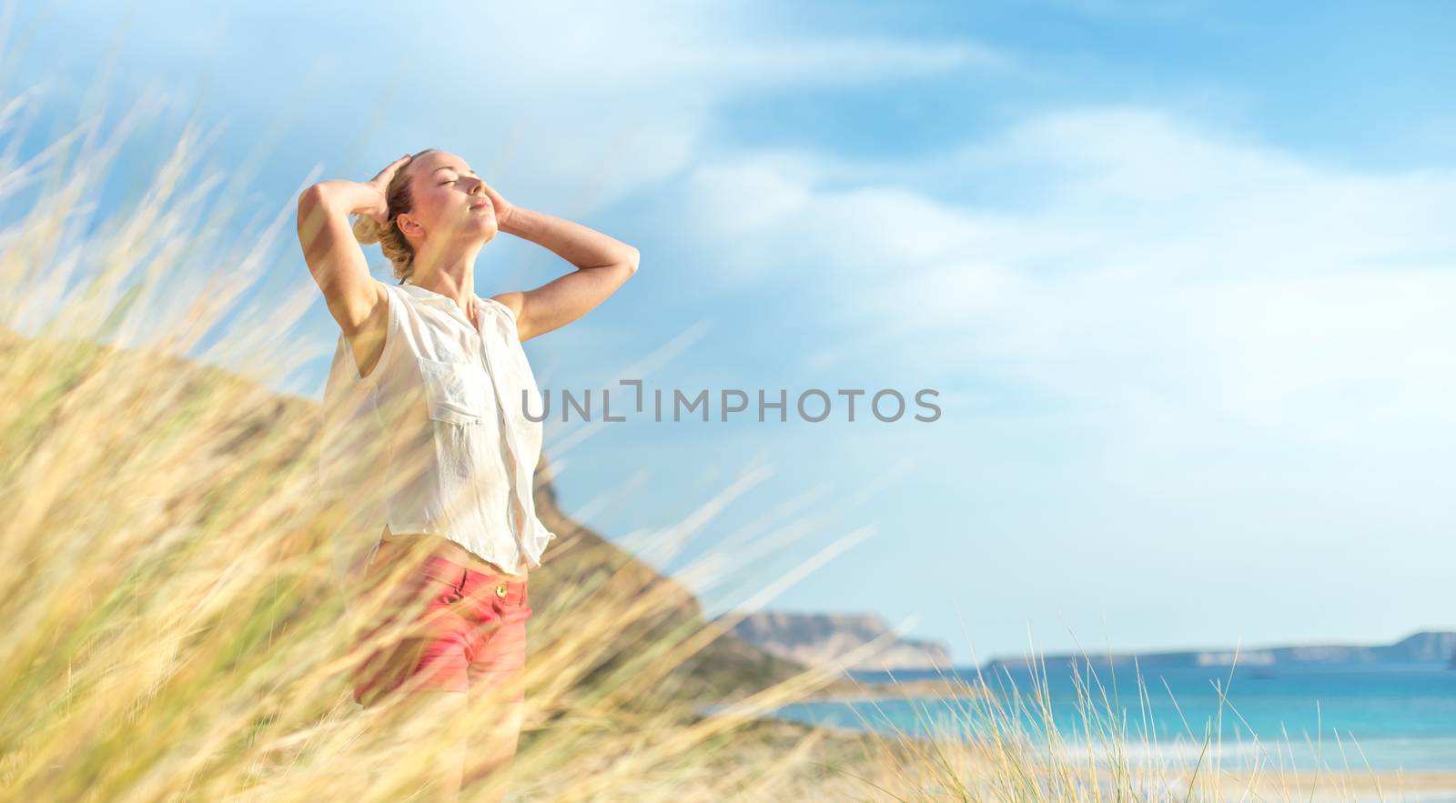 Relaxed woman, arms rised, enjoying sun, freedom and life an a beautiful beach. Young lady feeling free, relaxed and happy. Concept of vacations, freedom, happiness, enjoyment and well being.