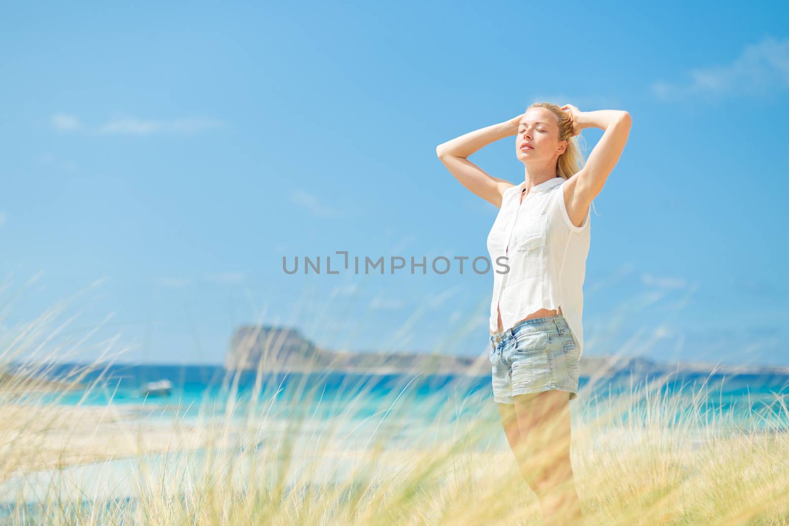 Relaxed woman, arms rised, enjoying sun, freedom and life an a beautiful beach. Young lady feeling free, relaxed and happy. Concept of vacations, freedom, happiness, enjoyment and well being.