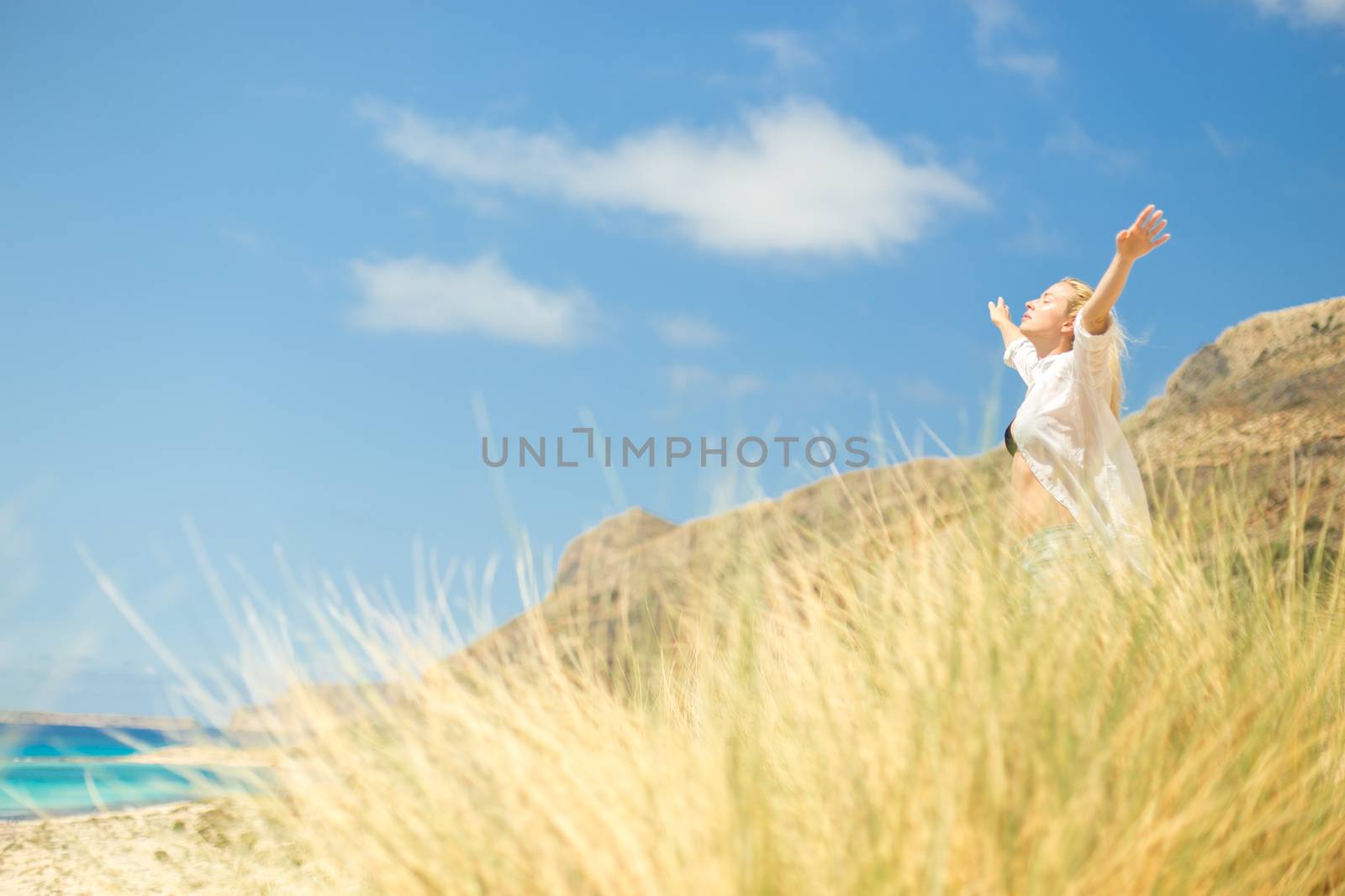 Relaxed woman, arms rised, enjoying sun, freedom and life an a beautiful beach. Young lady feeling free, relaxed and happy. Concept of vacations, freedom, happiness, enjoyment and well being.