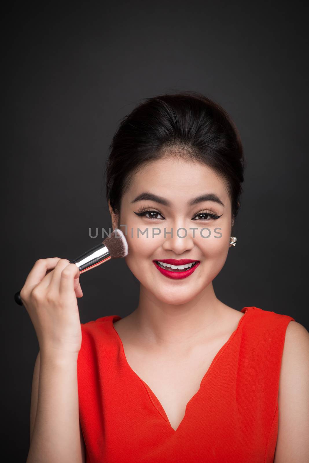 Cosmetic powder brush. Asian woman applying blusher on her cheeks with perfect make-up and red lips