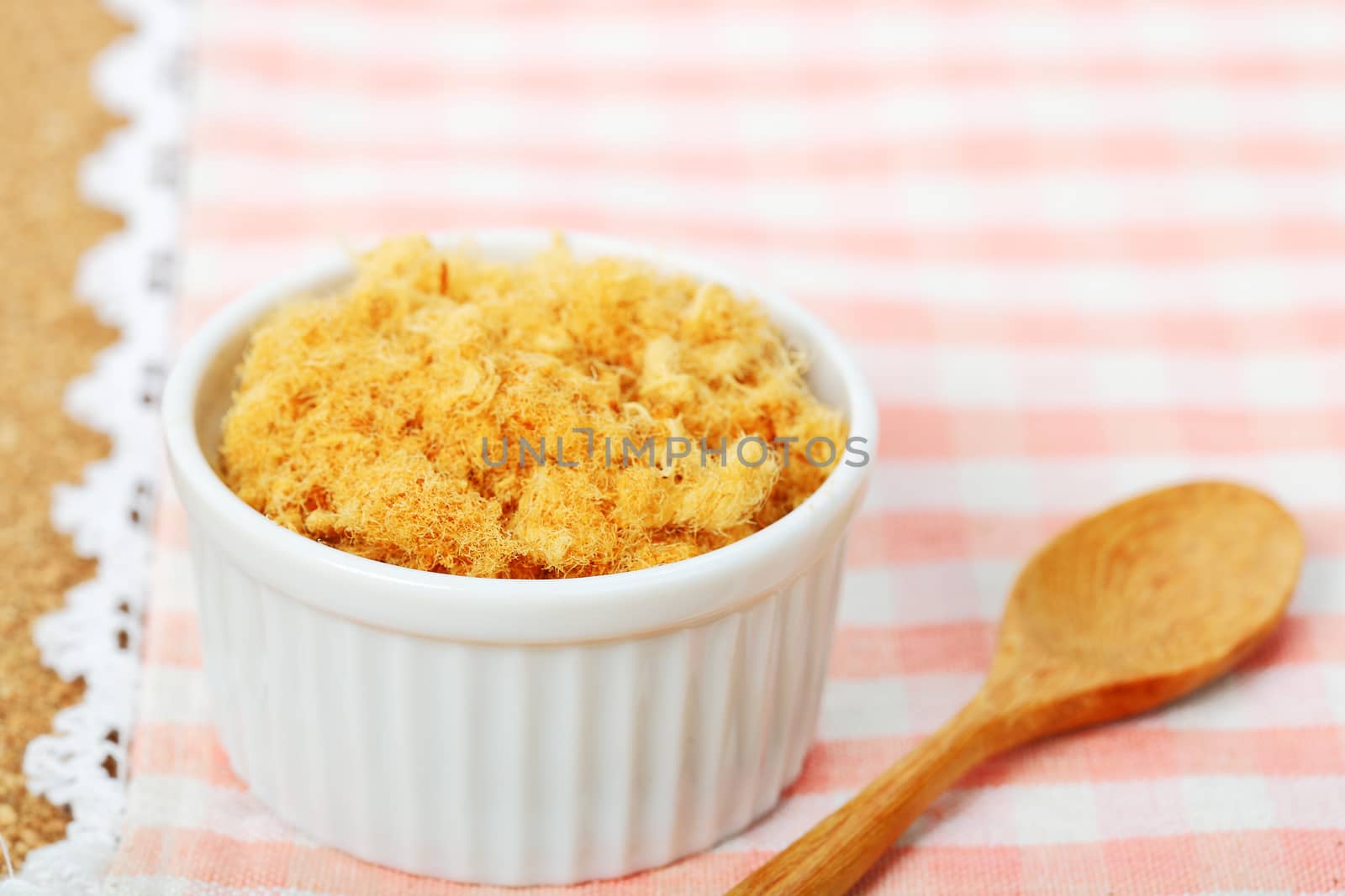 dried pork floss in white cup with wooden spoon on napery background.       