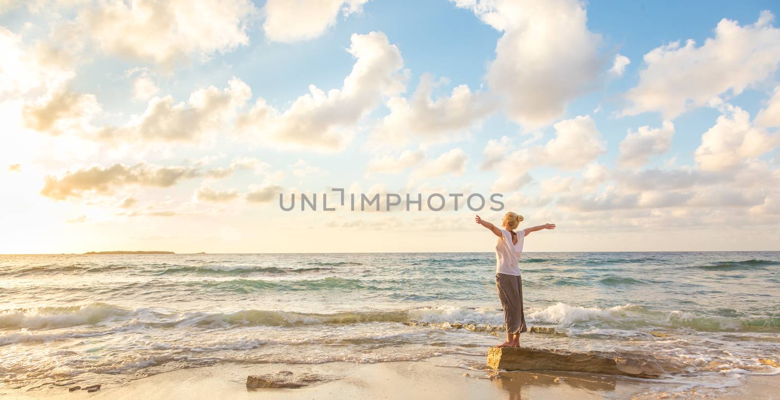 Relaxed woman enjoying sun, freedom and life an beautiful beach in sunset. Young lady feeling free, relaxed and happy. Concept of vacations, freedom, happiness, enjoyment and well being.