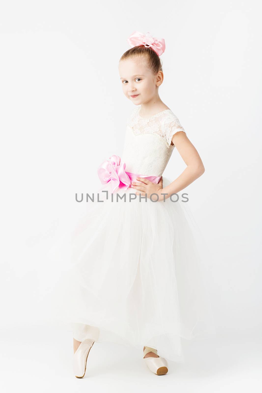 Beautiful ballet dancer on white background. Slender little ballerina girl in white dress and in pointe shoes