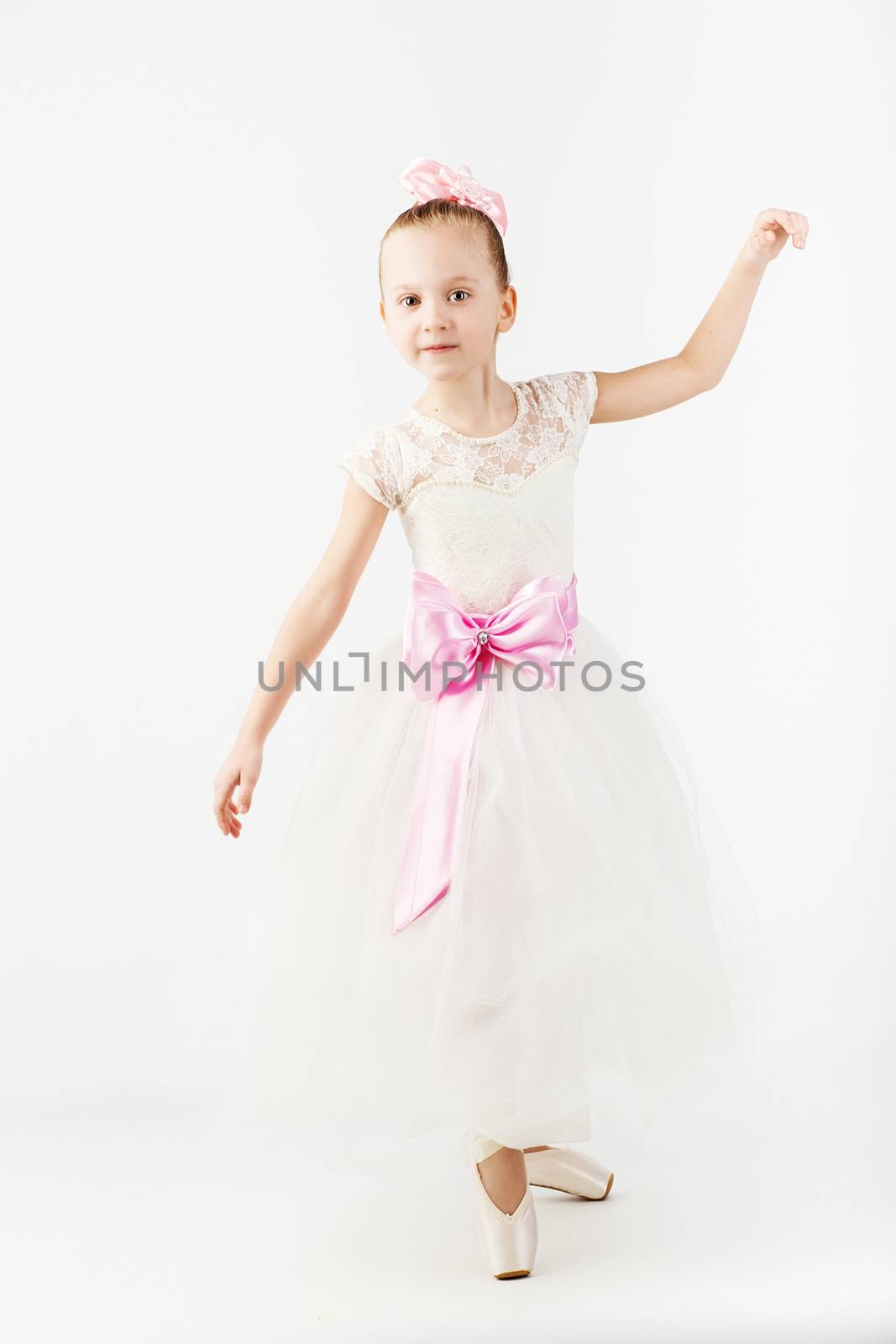 Beautiful ballet dancer isolated on white background. Slender little ballerina girl in white dress and in pointe shoes