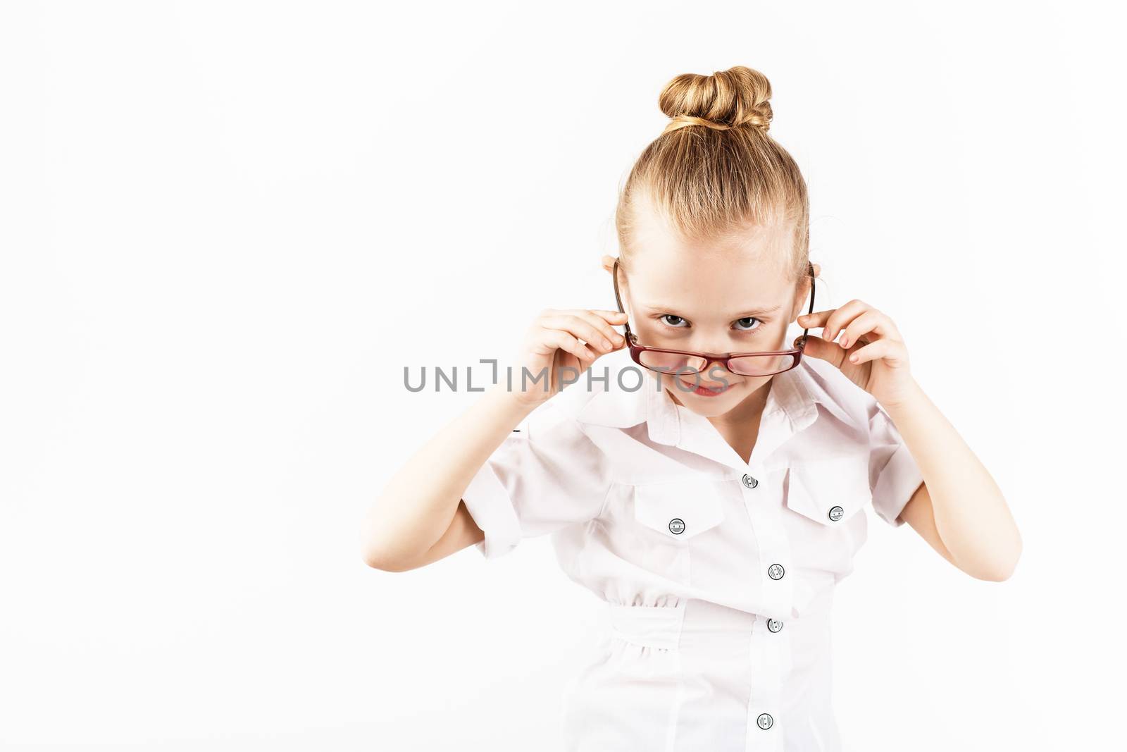 Funny little girl wearing eyeglasses imitates a strict teacher against white background. Little student Looking at camera. School concept. Back to School