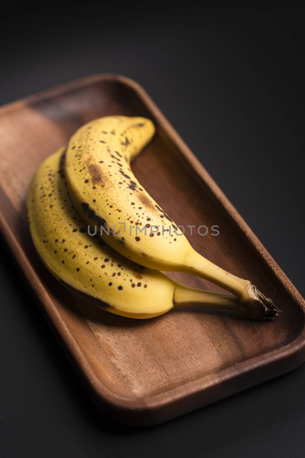Two organic bananas in a wood sish over a black board.