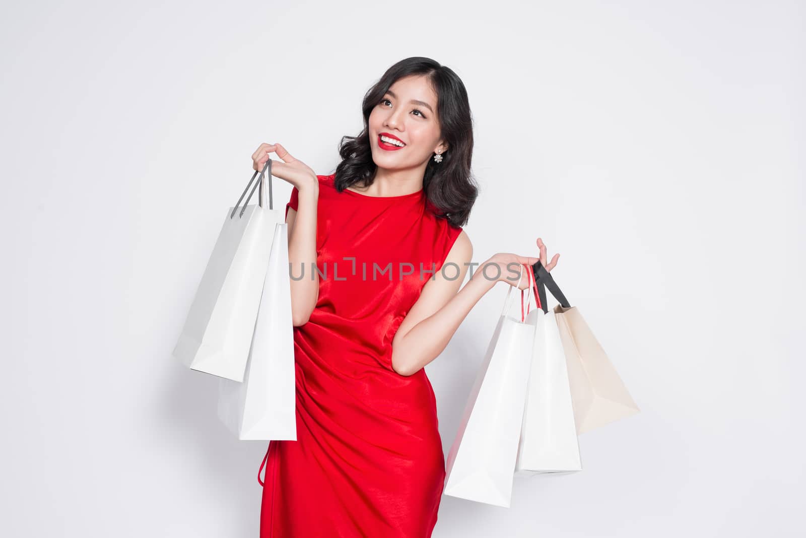 Cheerful fashionable asian woman wearing a red dress with shoppi by makidotvn