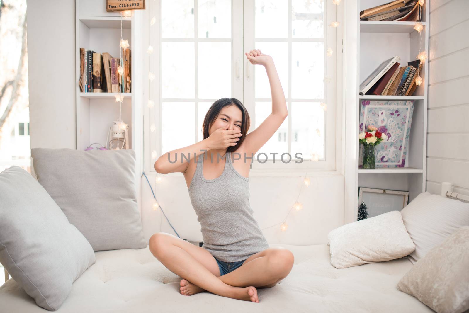 Tired sleepy asian woman waking up and stretching while sitting in bed at home
