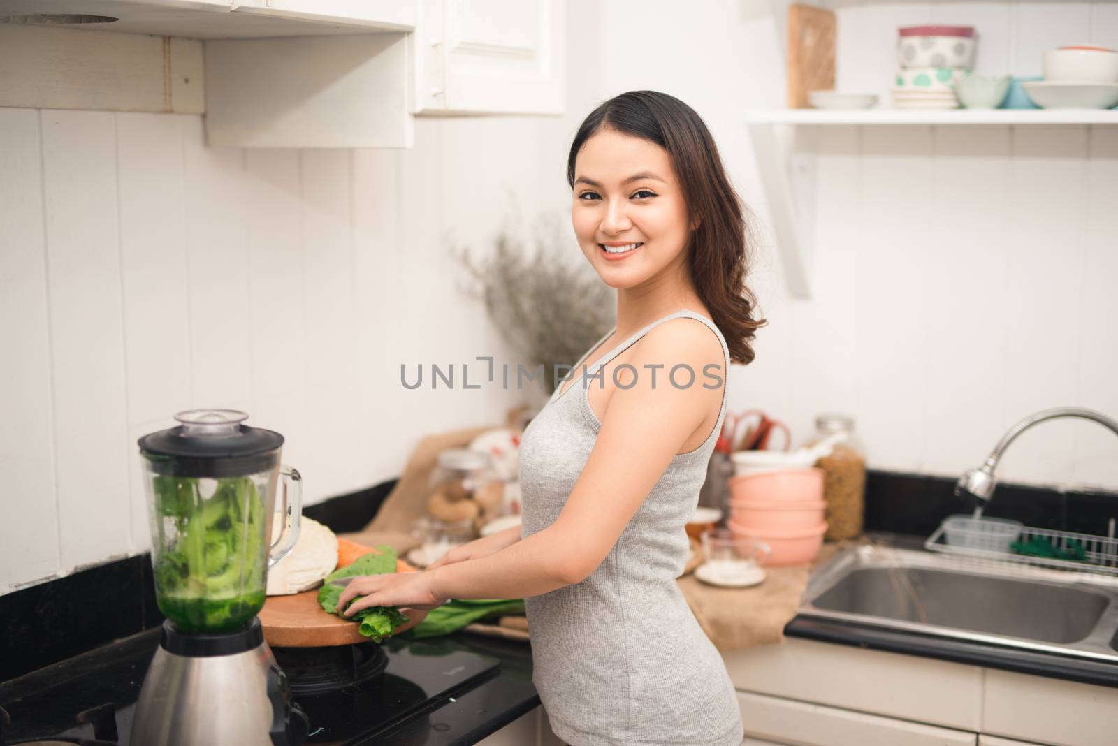 Smiling asian woman making smoothie with fresh vegetables in the by makidotvn