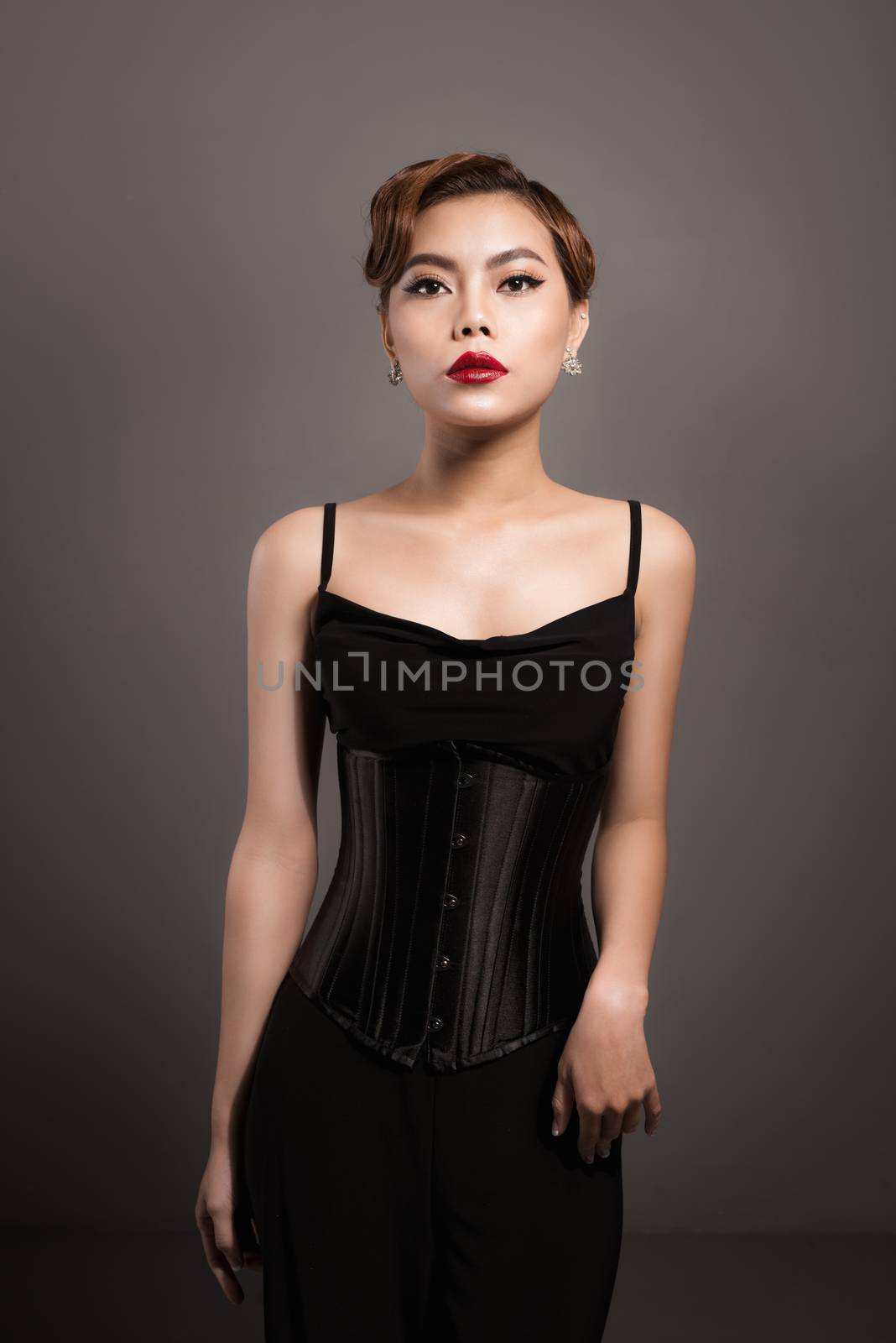 Sexy attractive asian woman posing in fashionable black dress over grey background
