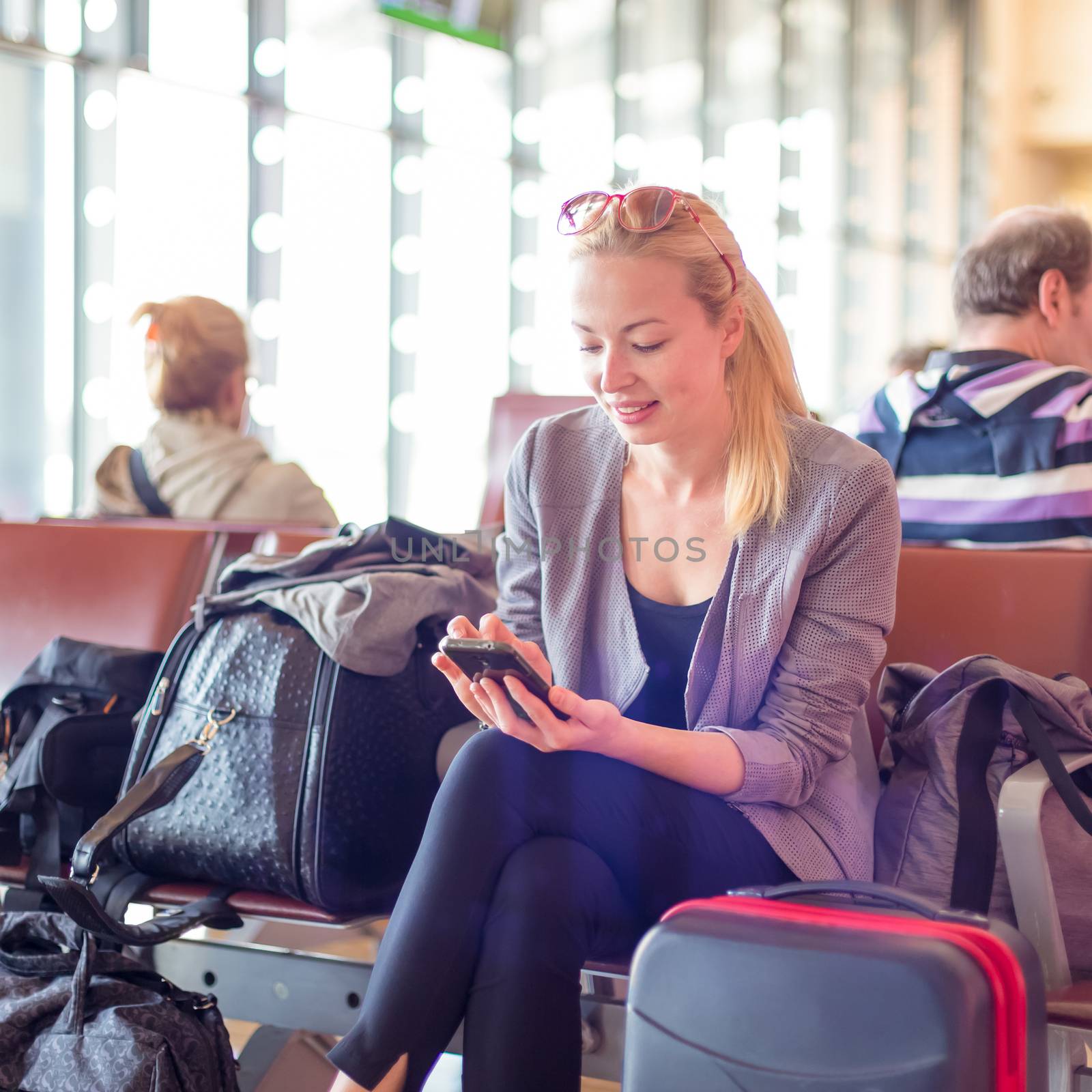 Casual blond young woman using her cell phone while waiting to board a plane at the departure gates. Wireless network hotspot enabling people to access internet conection. Public transport.