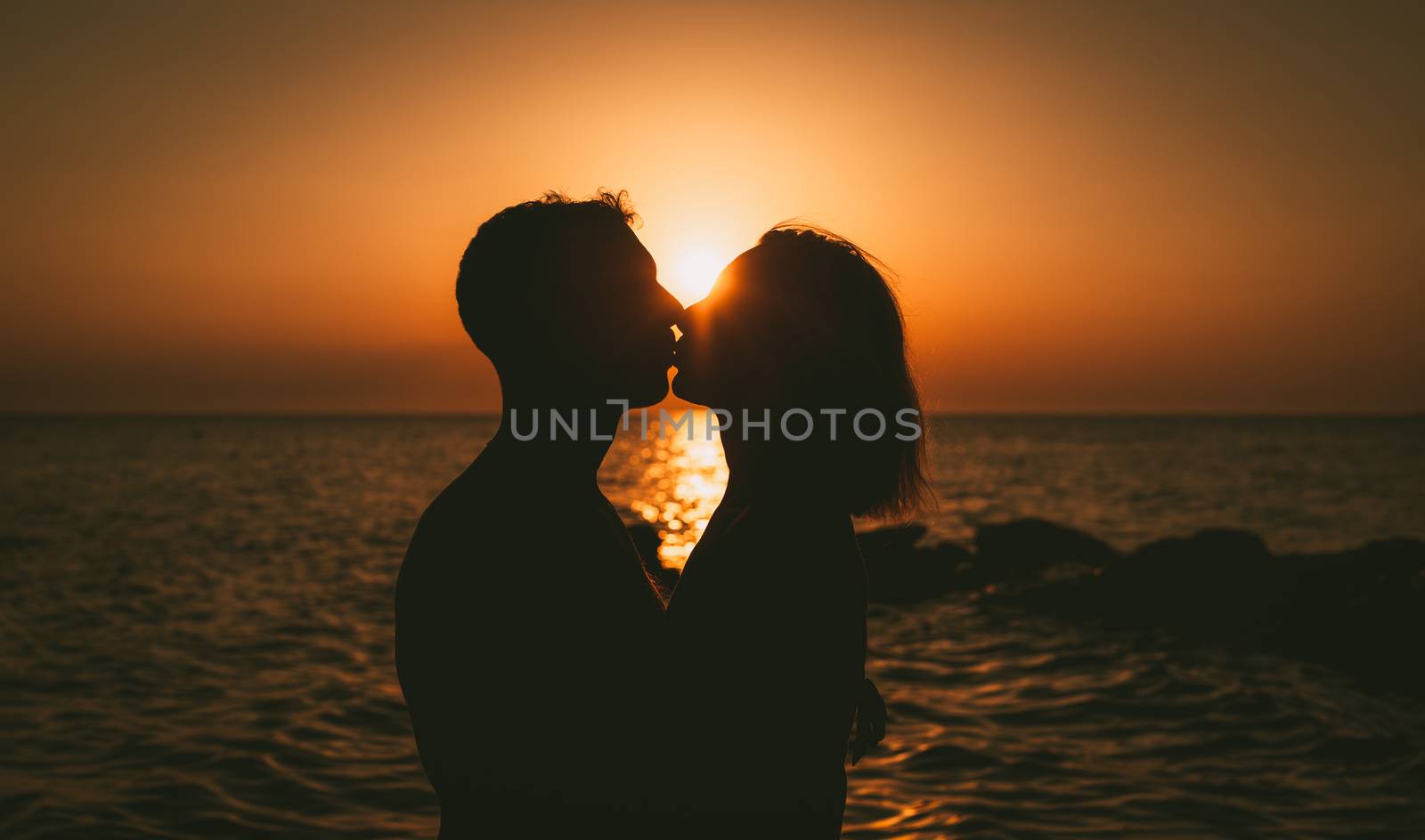 Silhouette of a loving couple hugging and kissing at sunset on the beach.