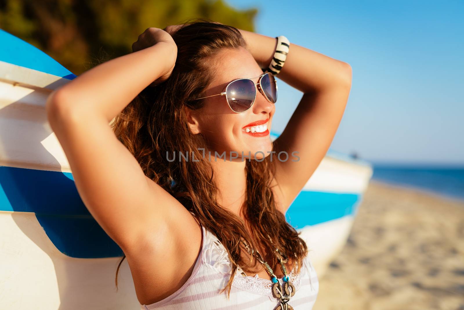 Beautiful young woman relaxing on the beach. She is sitting next to boat and enjoying at sunbathing.