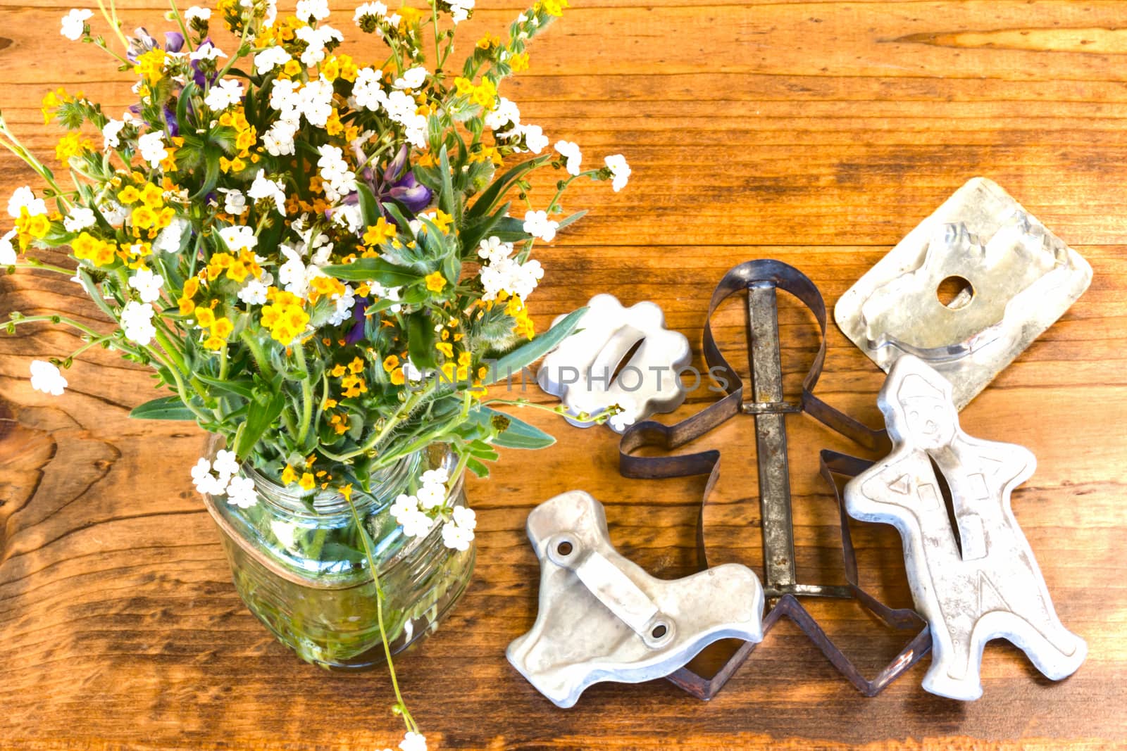 Tin Cookie Cutters and Flowers in Glass Vase Sitting on Wooden Table With Knots