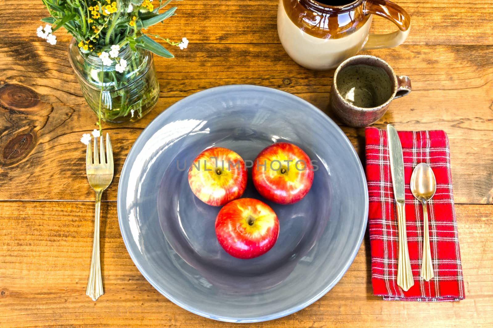 Place Setting With Red Apples Flowers and Crockery on Wooden Table With Knots