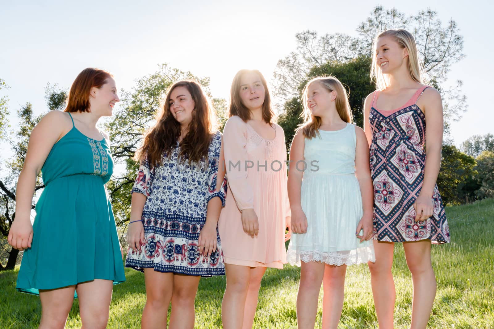 Young Girls Standing Together in Green Field With Trees in the Background and Sunlight Overhead