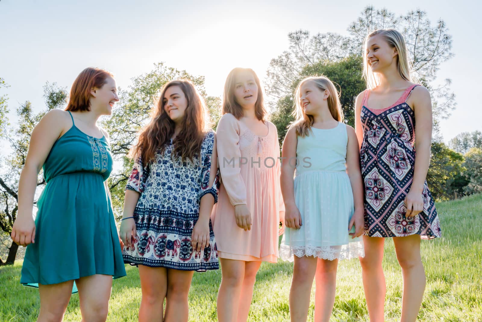 Young Girls Standing Together in Green Field With Trees in the Background and Sunlight Overhead