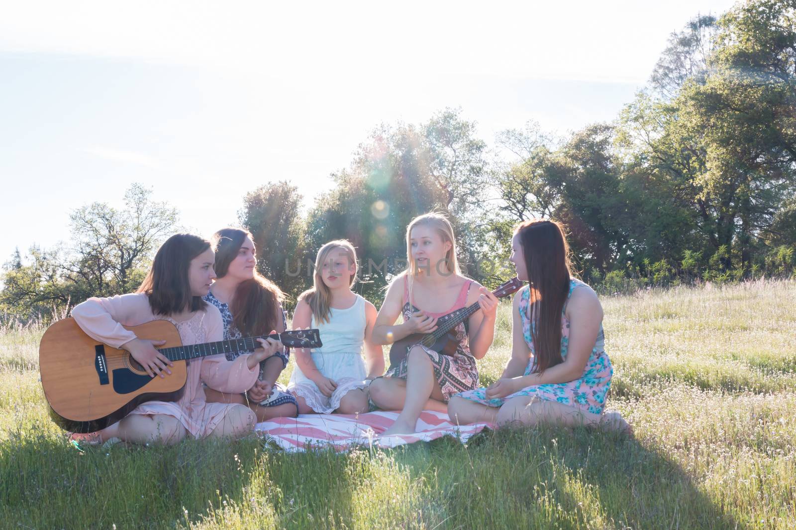 Young Girls Sitting Together in Grassy Field Singing and Playing Musical Instruments With Sunlight Overhead