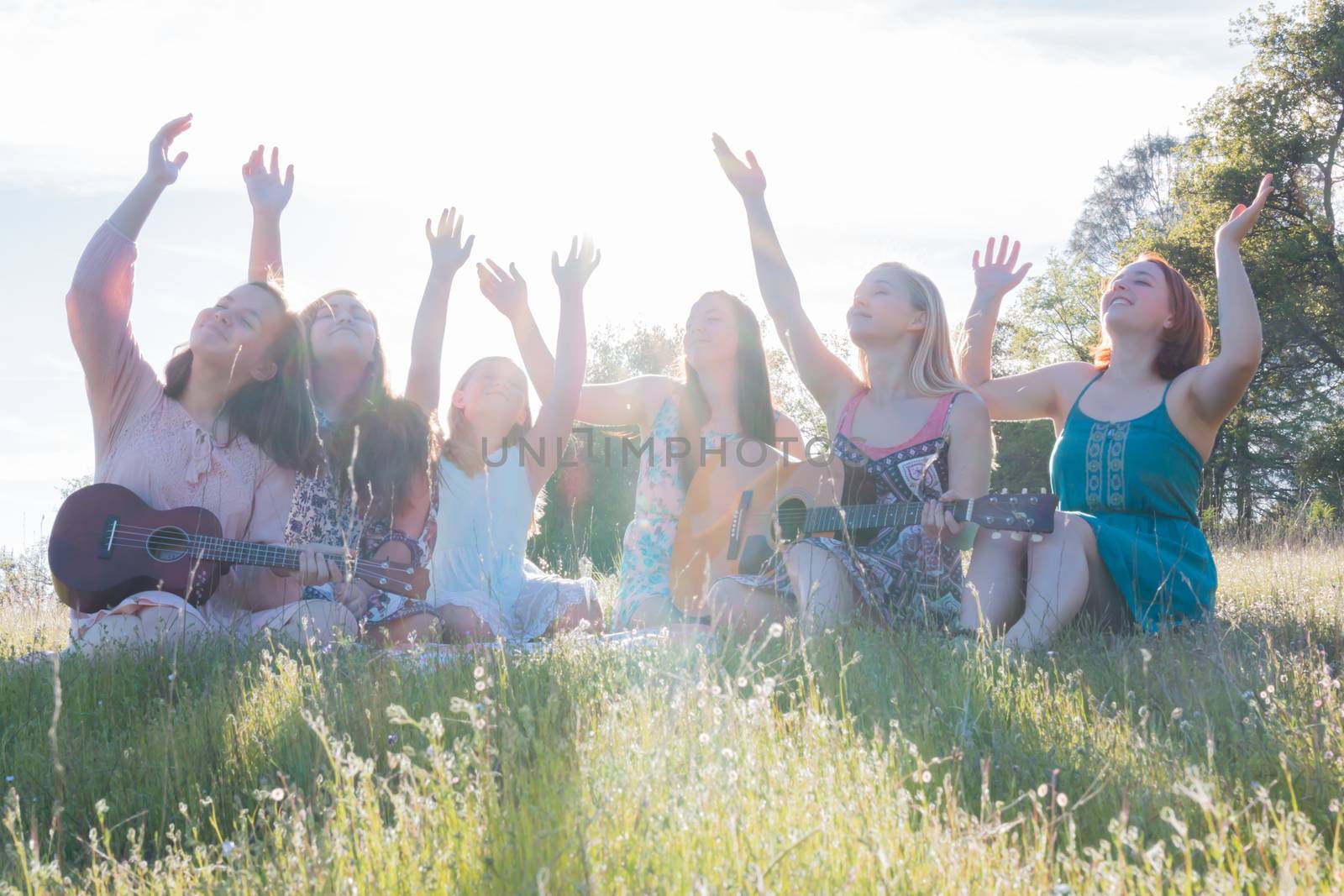 Young Girls Sitting Together in Green Grassy Field Singing and Playing Musical Instruments With Arms Raised up