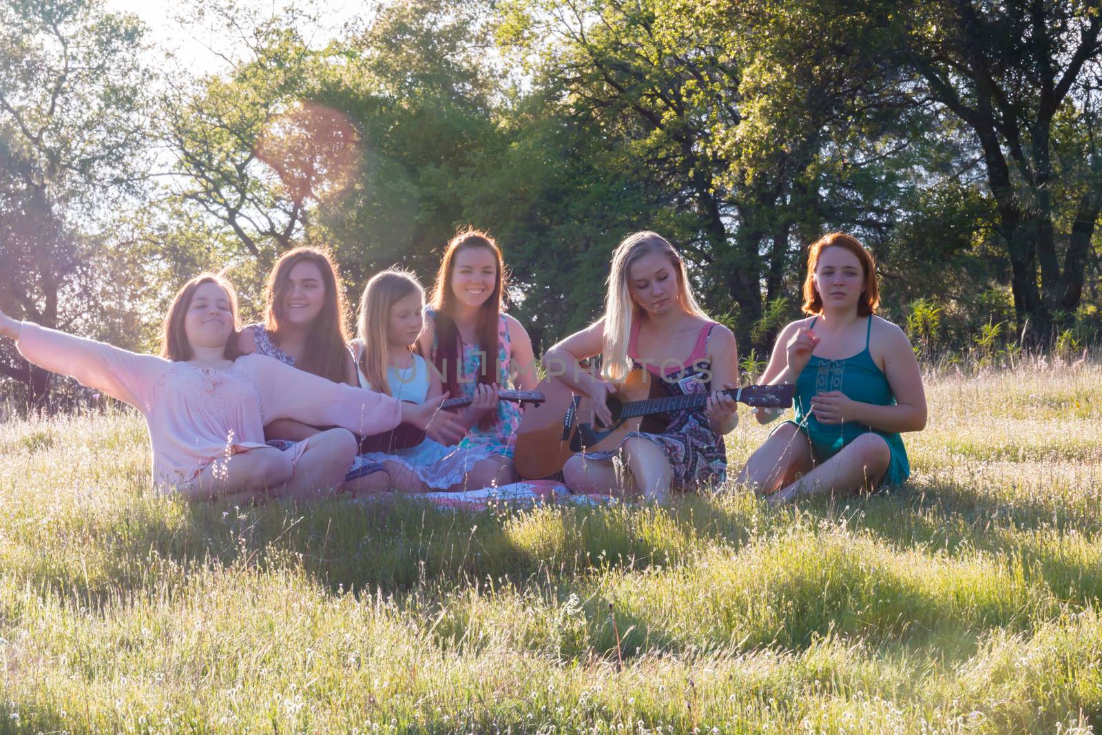 Young Girls Sitting Together in Grassy Field Singing and Playing Musical Instruments With Sunlight Overhead