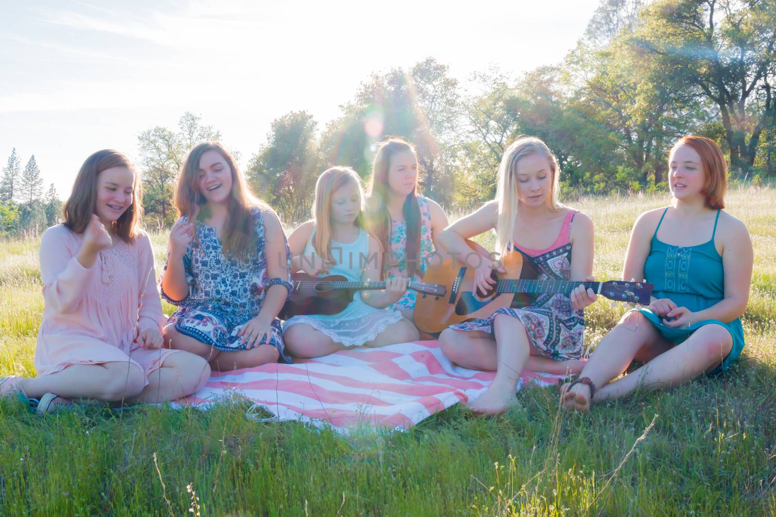 Young Girls Sitting Together in Grassy Field Singing and Playing Musical Instruments With Sunlight Overhead