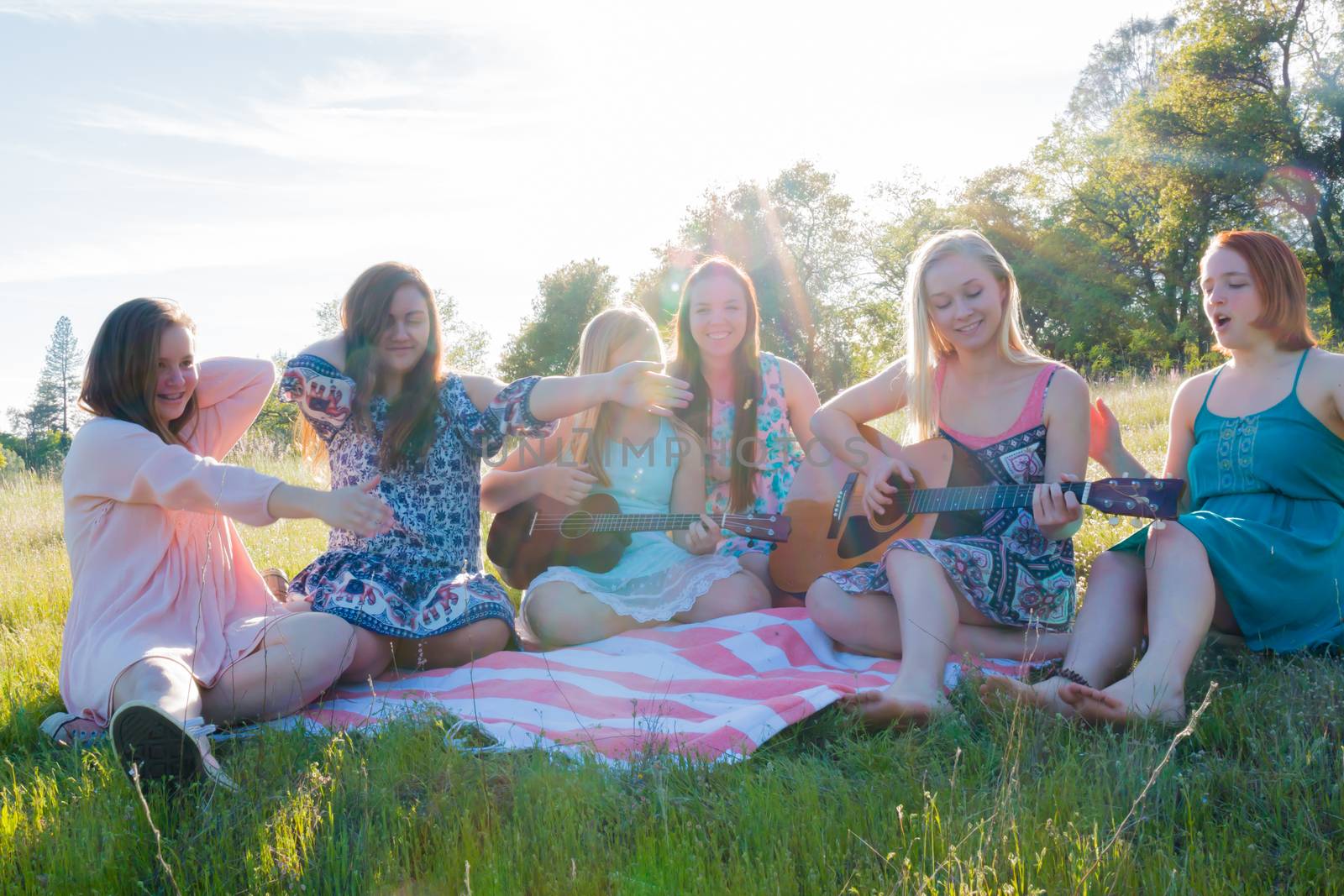 Young Girls Sitting Together in Grassy Field Singing and Playing Musical Instruments With Sunlight Overhead