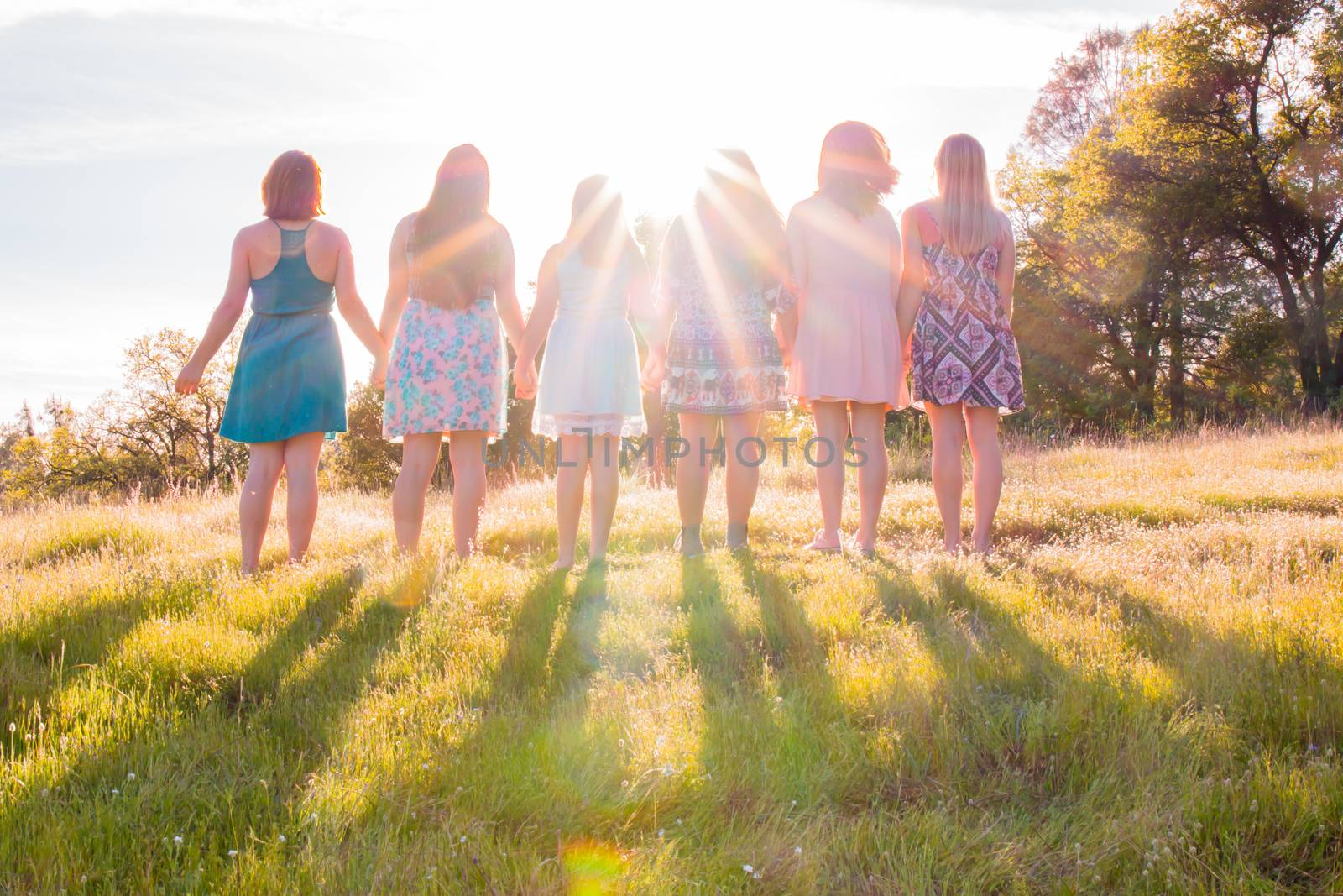 Young Girls Standing Together in Grassy Field Facing the Bright Sunset