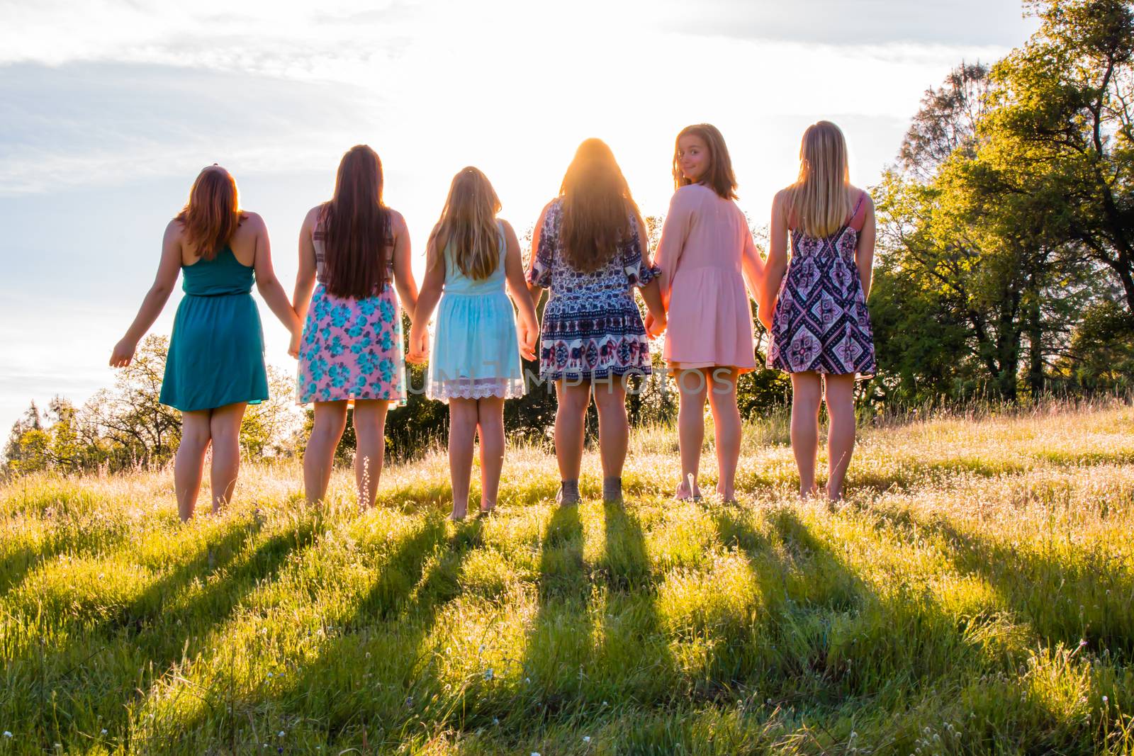 Young Girls Standing Together in Grassy Field Facing the Bright Sunset