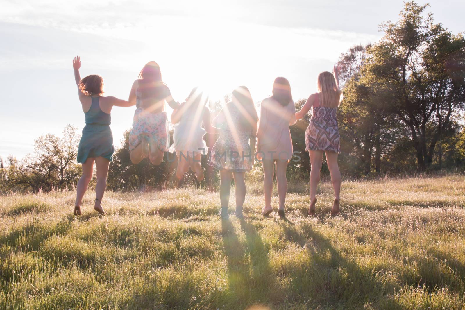 Girls Standing and Jumping Together Facing the Bright Sunset