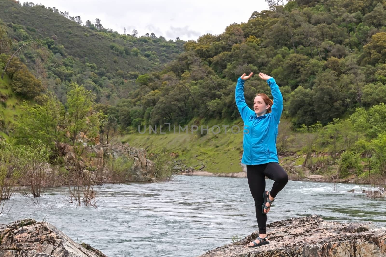 Young Girl Stretching on Rocks Near Fast River