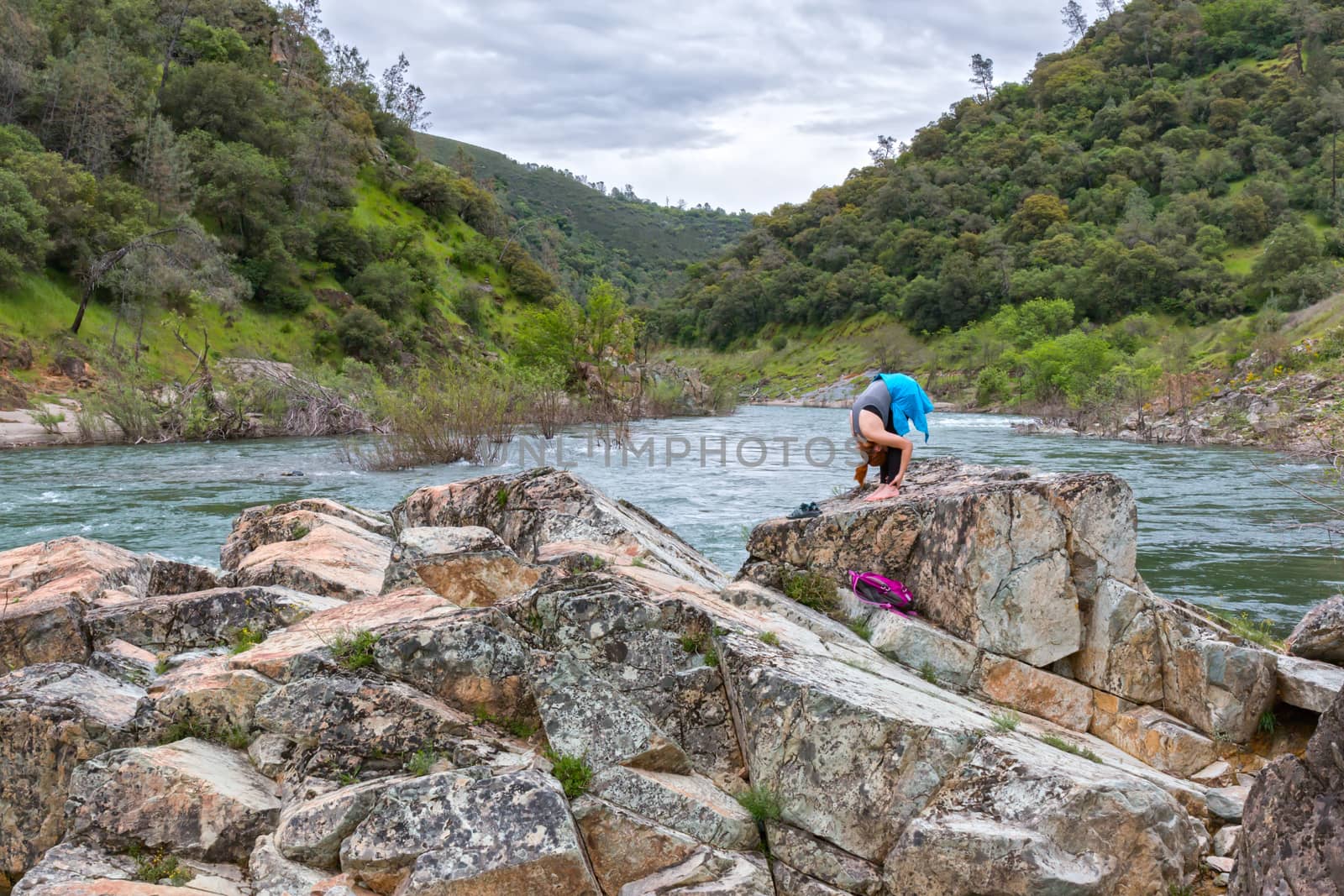 Young Girl Stretching on Rocks Near Fast River