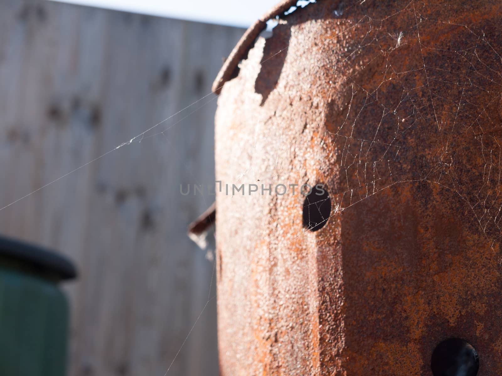 a thin spiderweb on the side of some rusted metal in light outside in the field in spring detail no spider