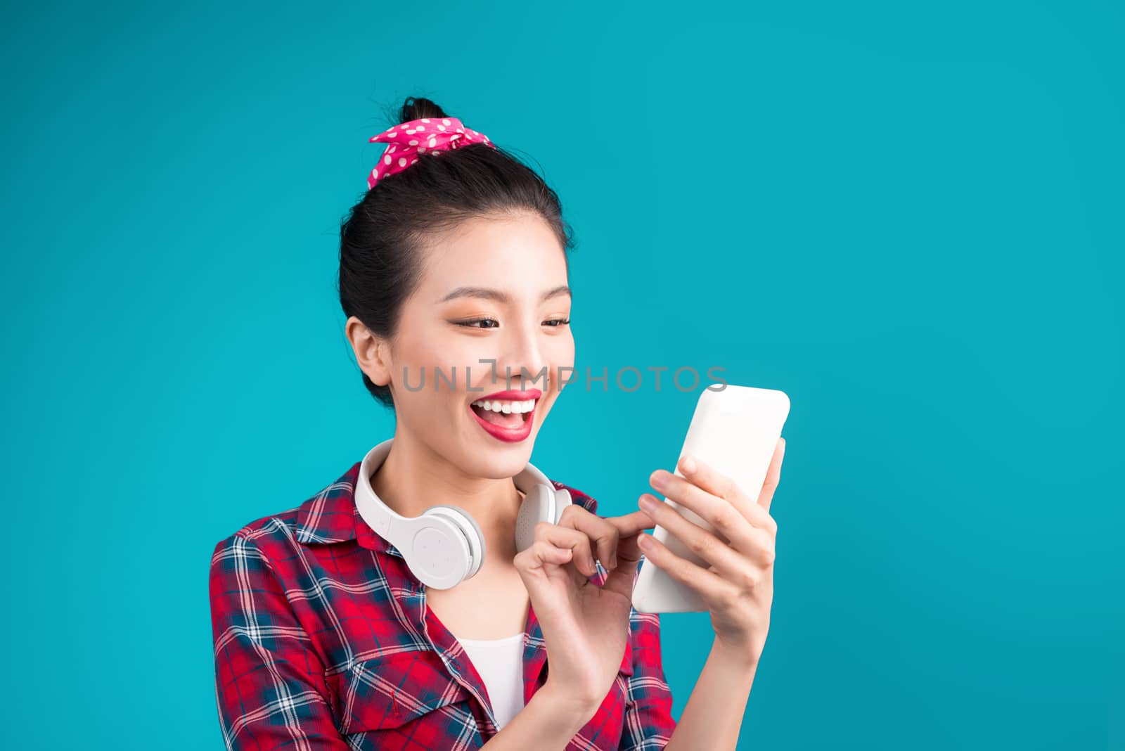 Happy young asian woman using smartphone standing over blue.