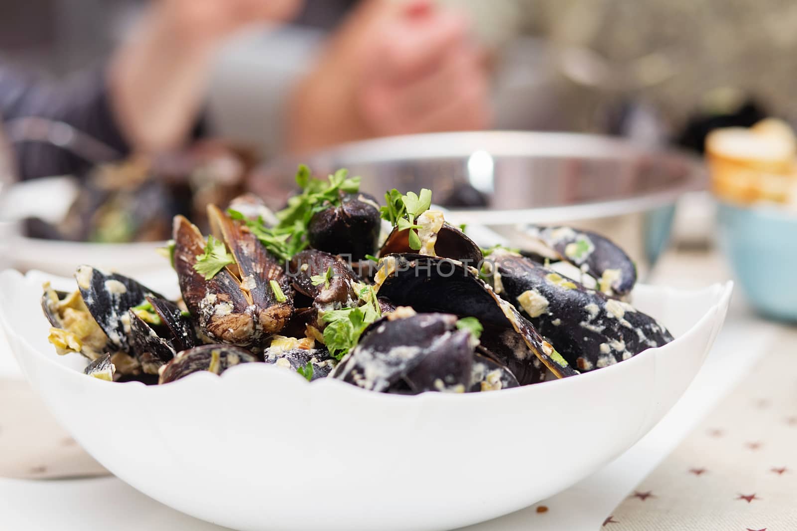 Steamed mussels in cheese sauce. Mussels in shells in the bowl with white wine on the table.