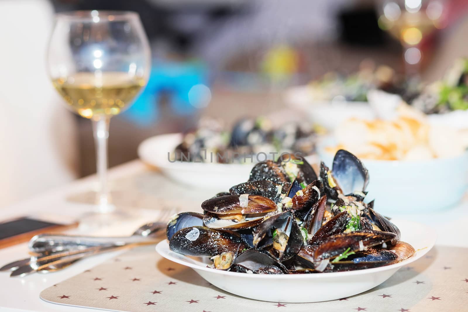 Steamed mussels in cheese sauce. Mussels in shells in the bowl with white wine on the table.