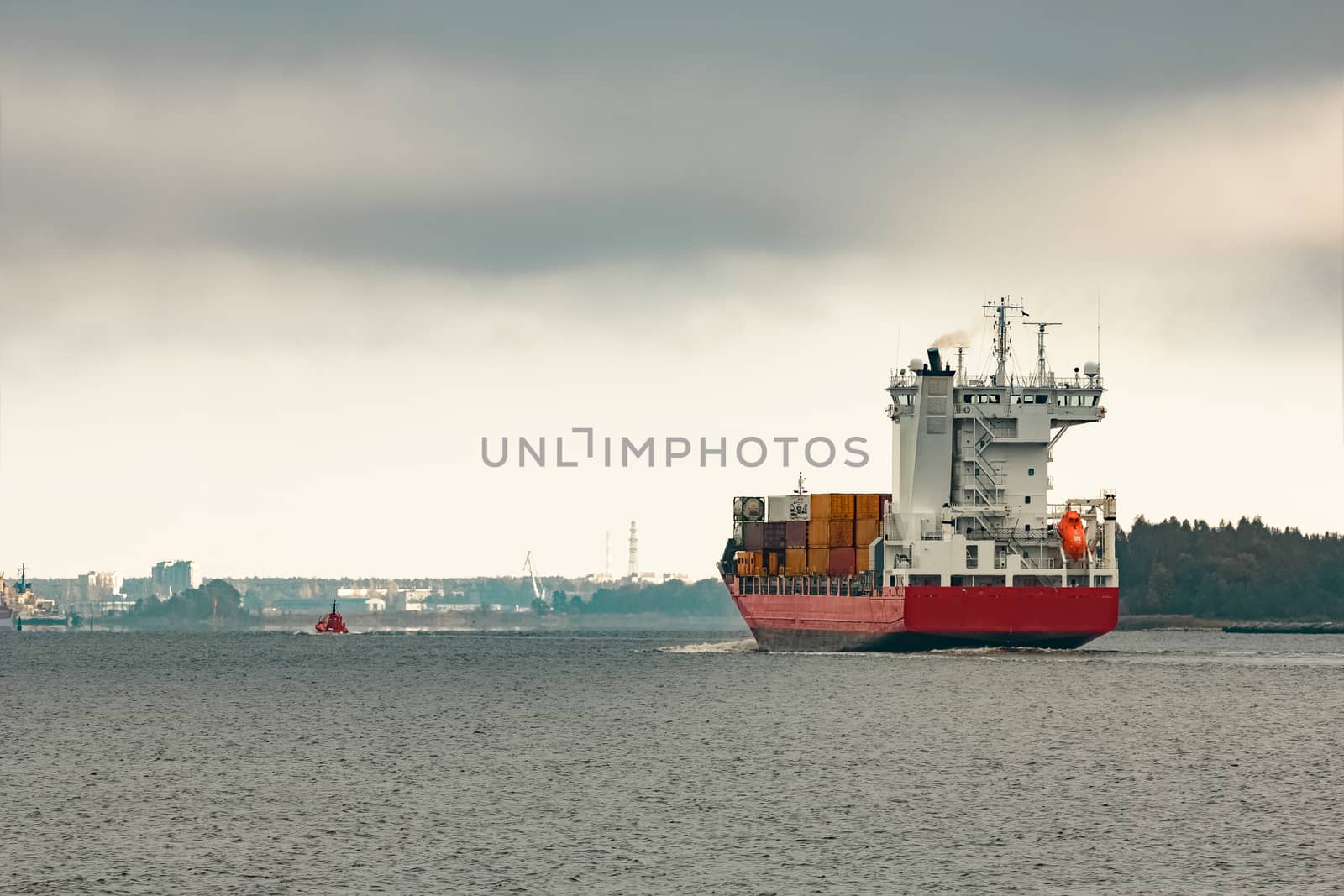 Red cargo container ship entering the port of Riga in cloudy day