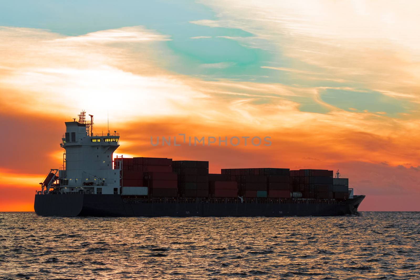 Blue container ship leaving Riga city during hot sunset