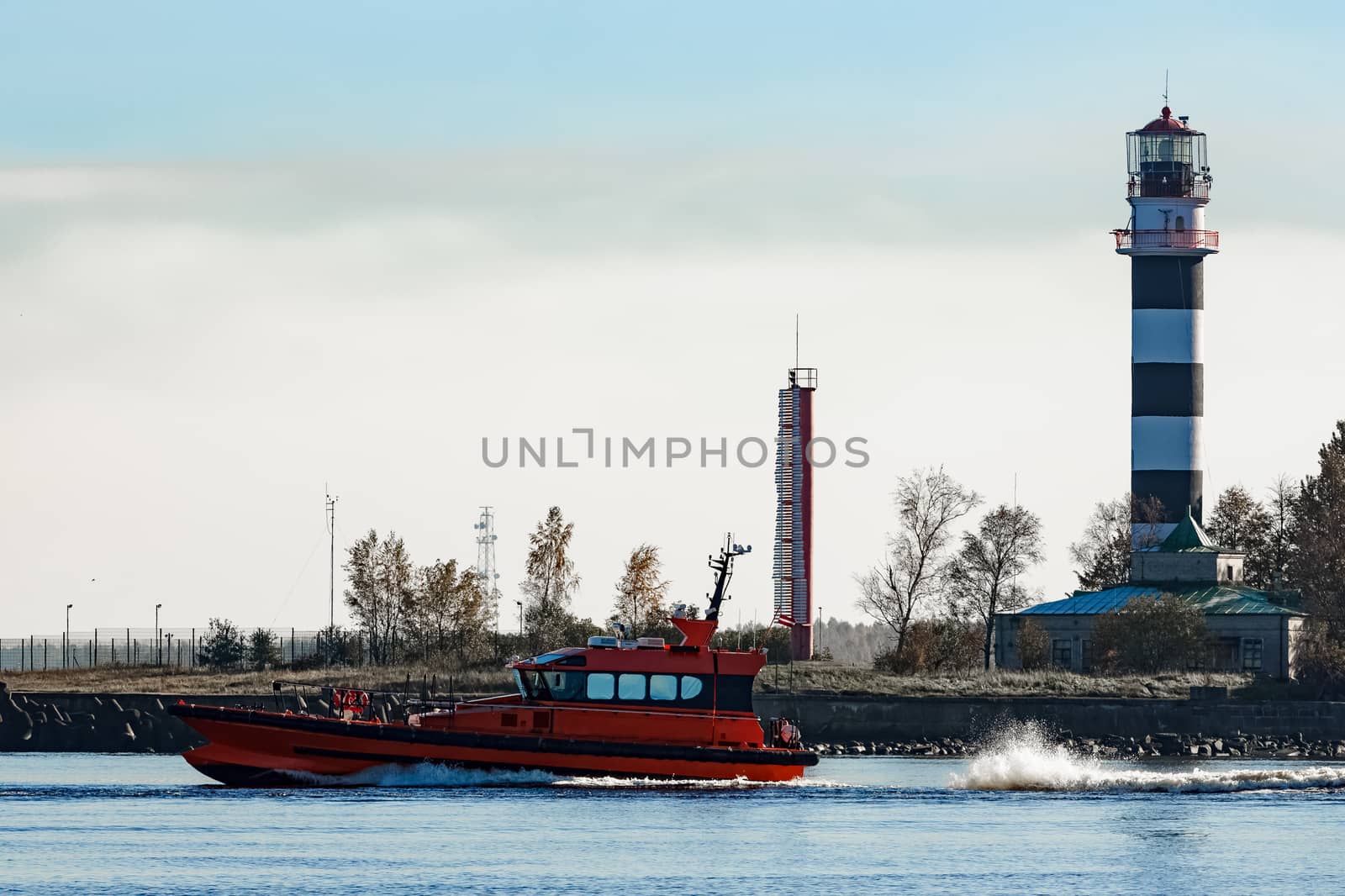 Red pilot ship sailing past the lighthouse in Riga