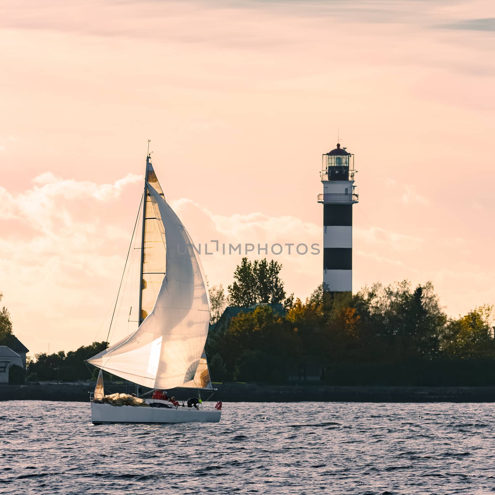 Sailboat moving past the big lighthouse in evening, Latvia