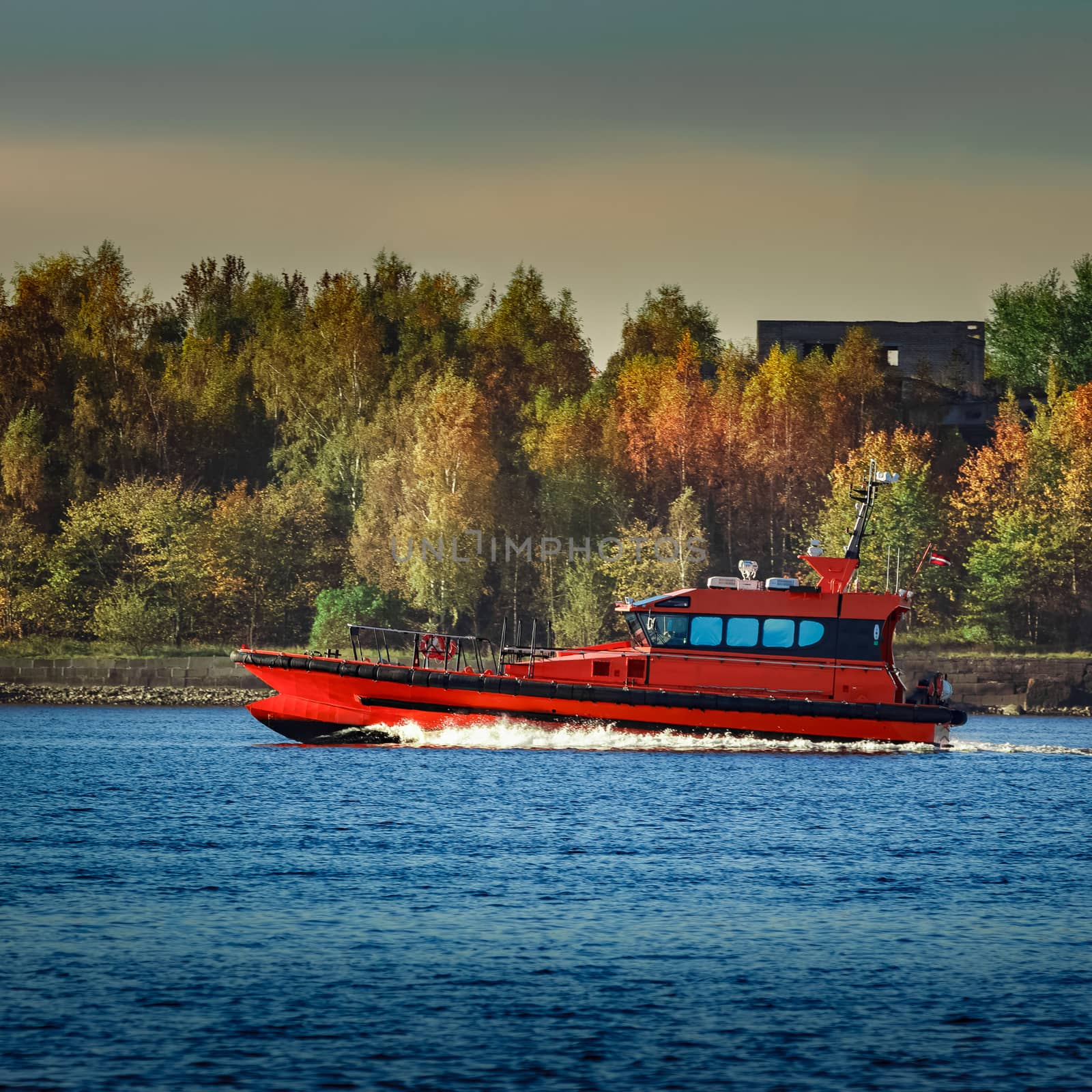 Red pilot ship moving past the autumn trees in Europe