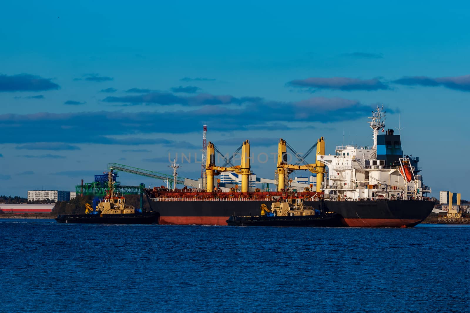 Black cargo ship mooring at the port with tug ship support