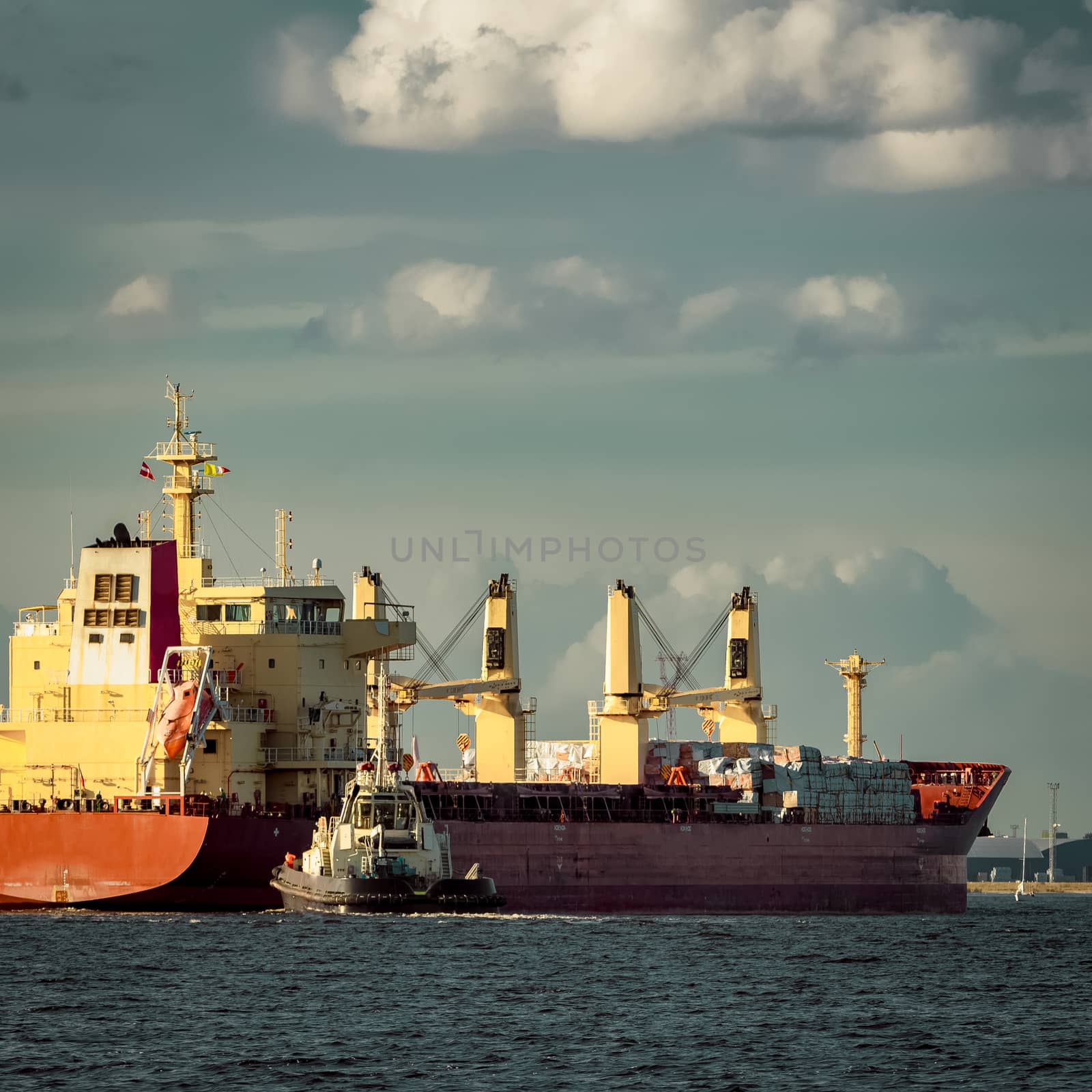 Red cargo ship and the tug ship towing it to the port