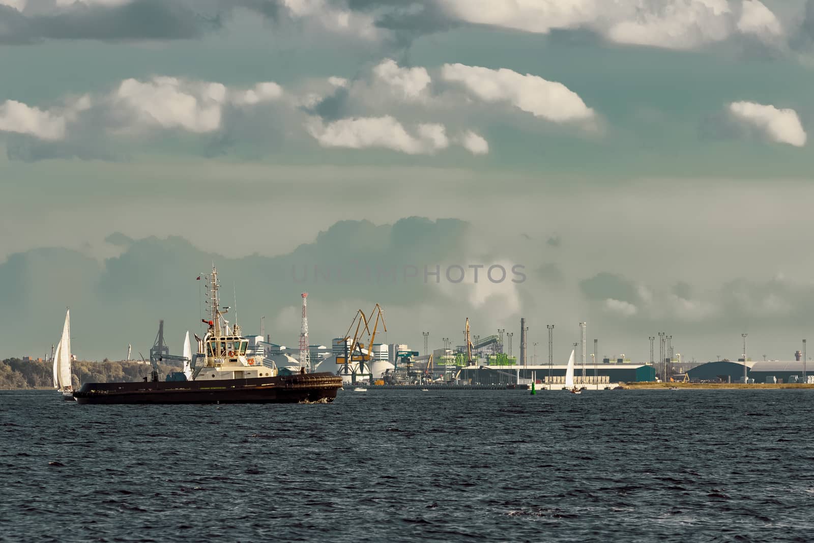 Tug ships and sailboats against cargo terminal in Riga