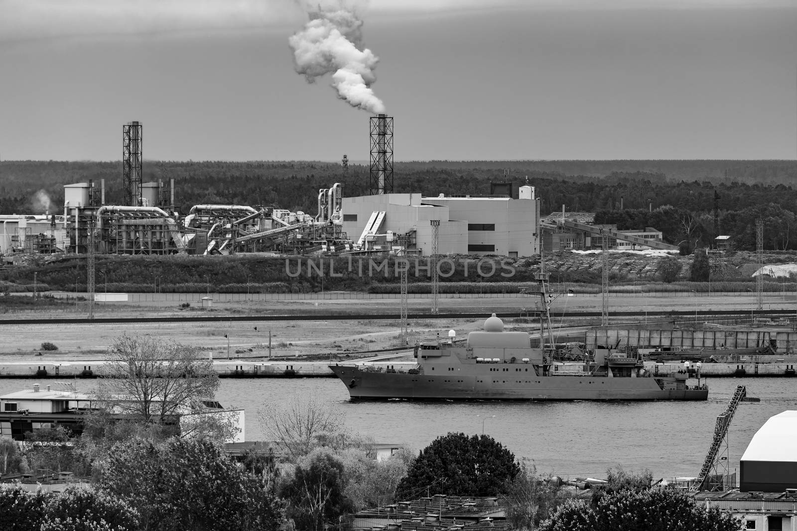 Military ship sailing past the cargo port in Latvia. Monochrome